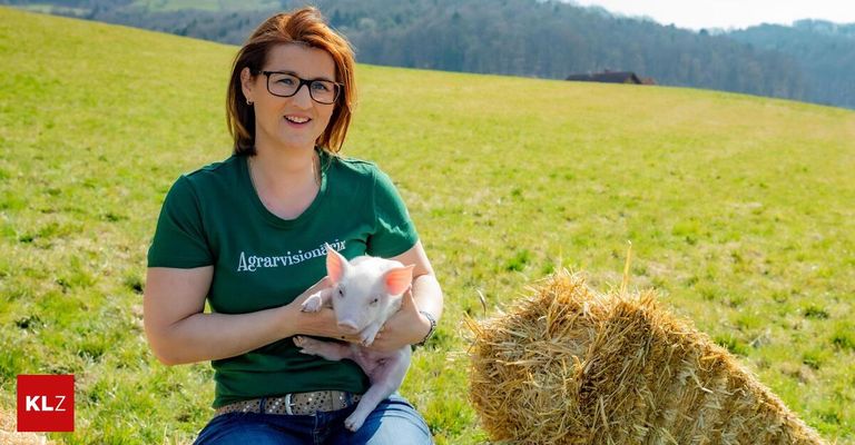 A woman wearing a green shirt with the word 'Agarvision' holds a small pig in a green field with a haystack nearby.
