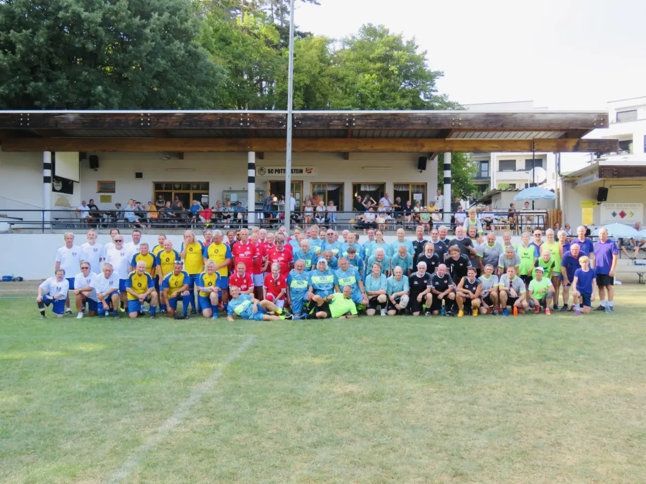 Eine große Gruppe von Menschen in Sportuniformen posiert für ein Foto auf einem Rasenfeld vor einem Gebäude mit einem Schild, das SC Pottstein liest.