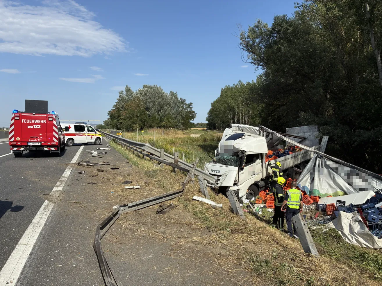 Ein Lkw-Unfall auf einer Autobahn mit Rettungsfahrzeugen und Personal, die den Unfallort abarbeiten. Der Lkw ist umgekippt und seine Ladung ist verstreut.