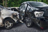 Zwei beschädigte Autos stehen auf der Straße, eines mit zerquetzter Front und das andere mit verbogenem Stoßfänger, beide in Schwarz und Silber.