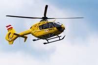 Ein gelber Hubschrauber mit einer rot-weißen Flagge an der Seite fliegt am Himmel.