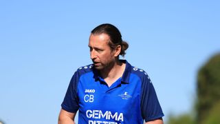 Ein Mann mit einem Pferdeschwanz, der ein blaues Poloshirt mit weißen Texten und Logos trägt und nach links schaut.