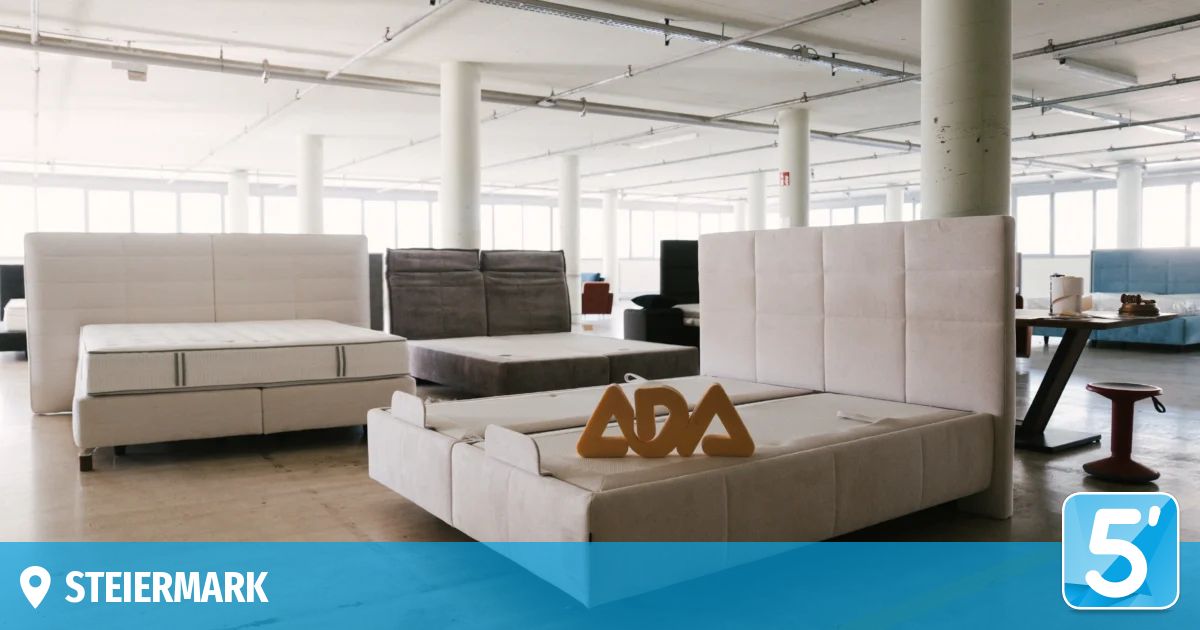 An empty warehouse with several beds and a large ADA sign on one of the beds. The warehouse has white walls and a high ceiling with metal beams.
