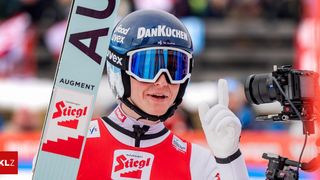 Ein Skifahrer mit einem DANKÜCHEN-Helm und einer Sonnenbrille zeigt nach einem erfolgreichen Lauf einen Daumen hoch. Das rote und weiße Trikot des Skifahrers hat das Wort Stiegl darauf.