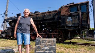 Ein älterer Mann steht neben einer alten Dampflokomotive mit einem Schild, das ihre Spezifikationen beschreibt.