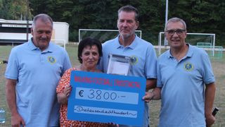 Eine Frau hält ein blaues Schild, auf dem Walking-Football Triestingtal und ein Betrag von 3800 Euro steht. Dahinter stehen drei Männer in hellblauen Poloshirts vor einem Fußballfeld.