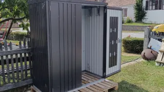 Ein schwarzer Lagerschuppen mit offener Tür, auf Holzpaletten im Garten platziert.