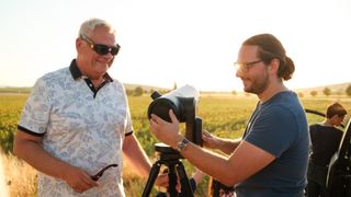 Zwei Männer stehen auf einem Feld, einer hält ein Teleskop und lächelt, während der andere es justiert.