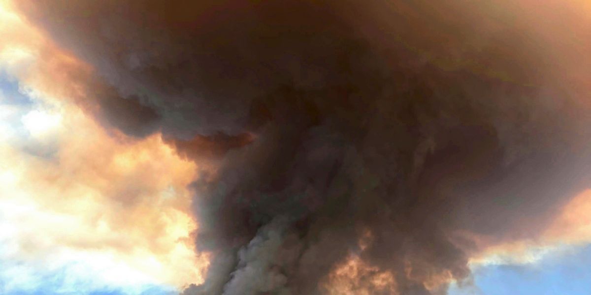A large plume of dark smoke rises against a backdrop of a partly cloudy sky, suggesting a significant fire or industrial activity.