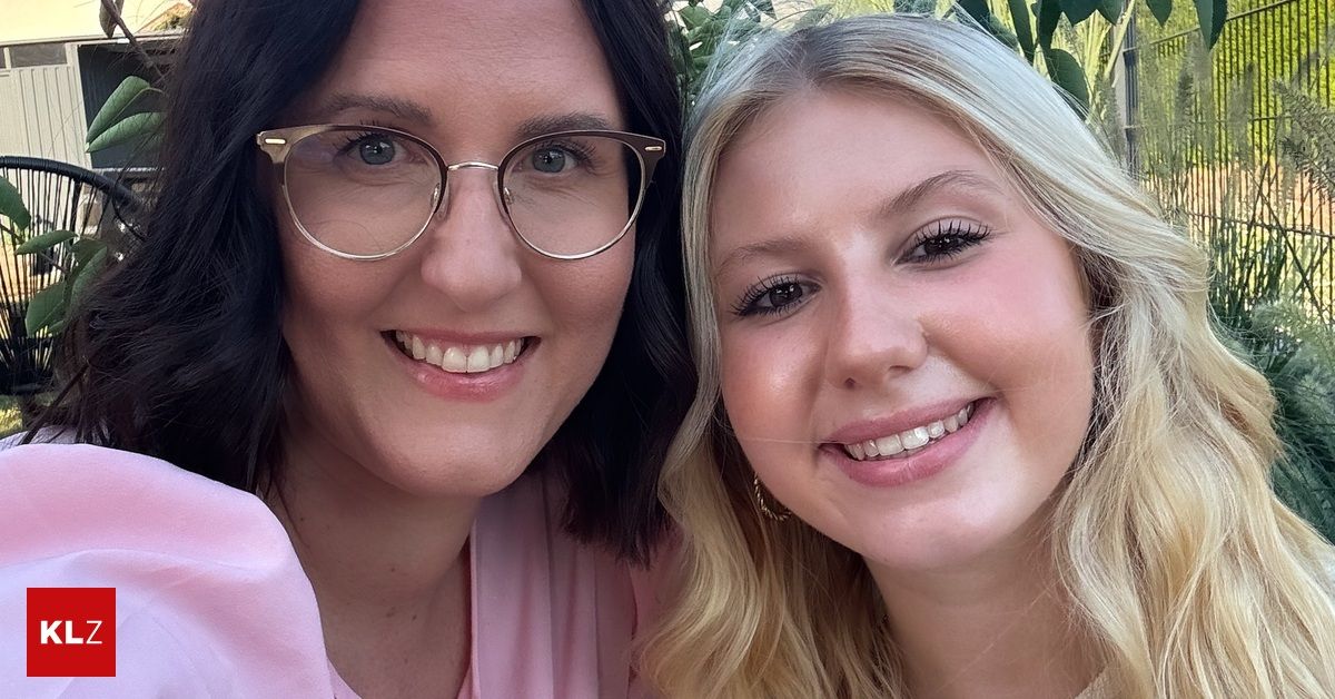 Two women smiling, one with glasses, both wearing pink. The woman on the right has blonde hair and is wearing earrings.