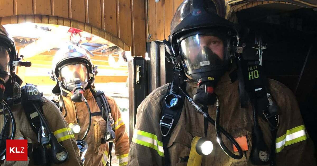 Zwei Feuerwehrleute in voller Ausrüstung, einer mit eingeschalteter Taschenlampe, stehen in einem hölzernen Raum.