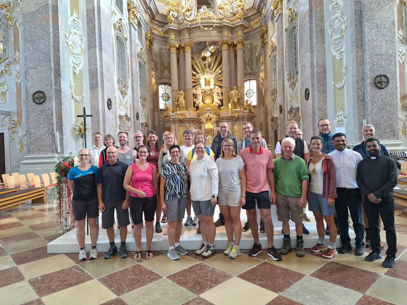 Eine Gruppe von Menschen steht vor einem kunstvollen Altar in einer Kirche und lächelt für ein Foto.