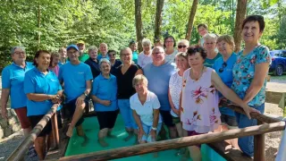 Eine Gruppe von Menschen, einige in Badekleidung, versammelt sich um einen kleinen Pool in einer Waldumgebung und posiert für ein Foto.