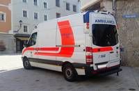 A white ambulance with red stripes is parked on the side of the street in front of a building.