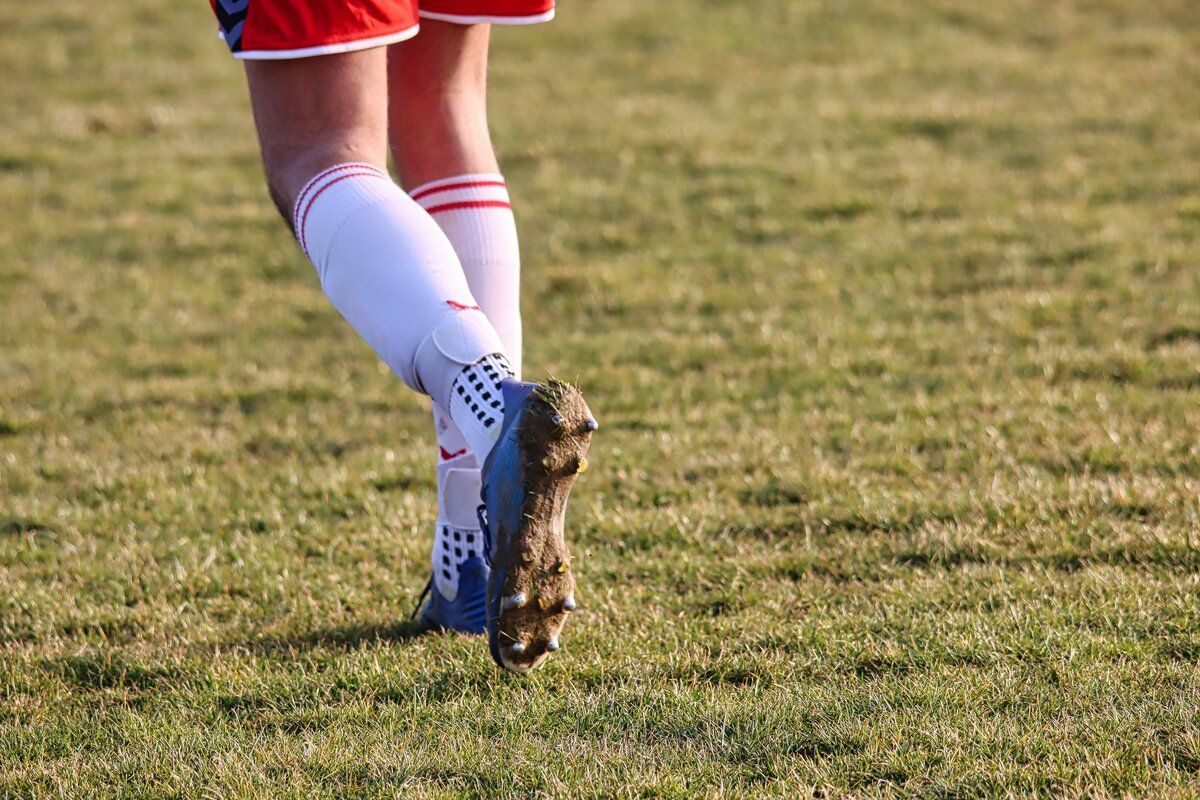 Der Fuß eines Fußballspielers mit einem schlammigen Fußballschuh auf einem Rasenfeld.