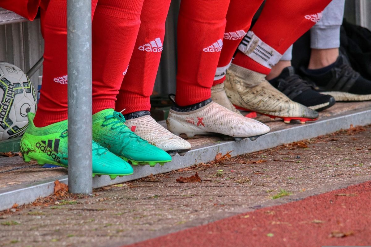 Close-up of soccer players' legs in red and green Adidas soccer cleats, standing on the edge of a track.