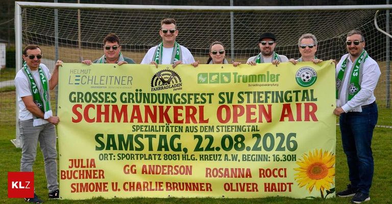 A group of people are standing behind a banner advertising a festival event in Germany. The banner features a yellow background with red and green text. The event is titled 'Grosses Grundungsfest SV Stiefital Schmankerl Open Air' and is scheduled for August 22, 2026.