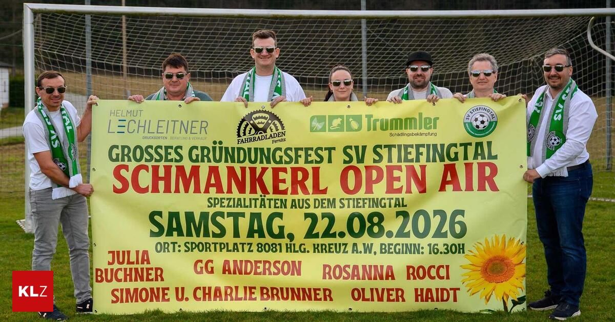 A group of people are standing behind a banner advertising a festival event in Germany. The banner features a yellow background with red and green text. The event is titled 'Grosses Grundungsfest SV Stiefital Schmankerl Open Air' and is scheduled for August 22, 2026.