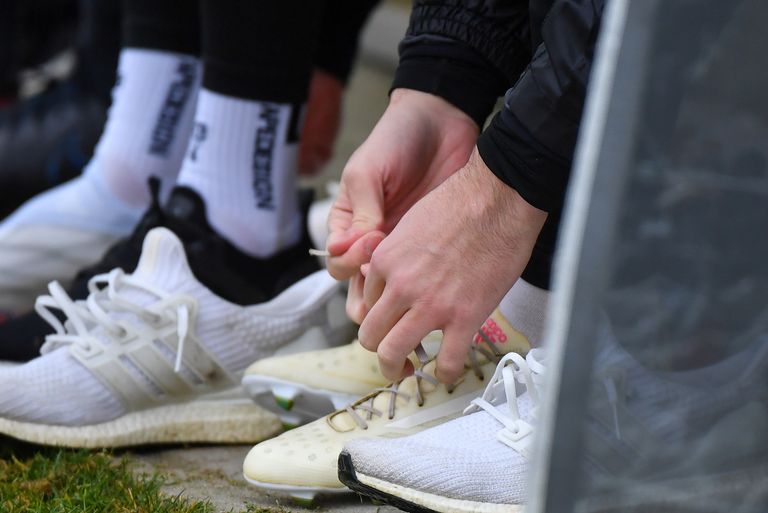 Eine Person bindet die Schnürsenkel einer anderen Person, die weiße Turnschuhe mit schwarzen Akzenten trägt.