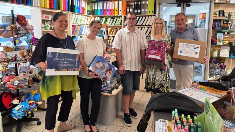 Five adults stand in a store with various gifts and books in the background. They are holding gifts and smiling for a photo.