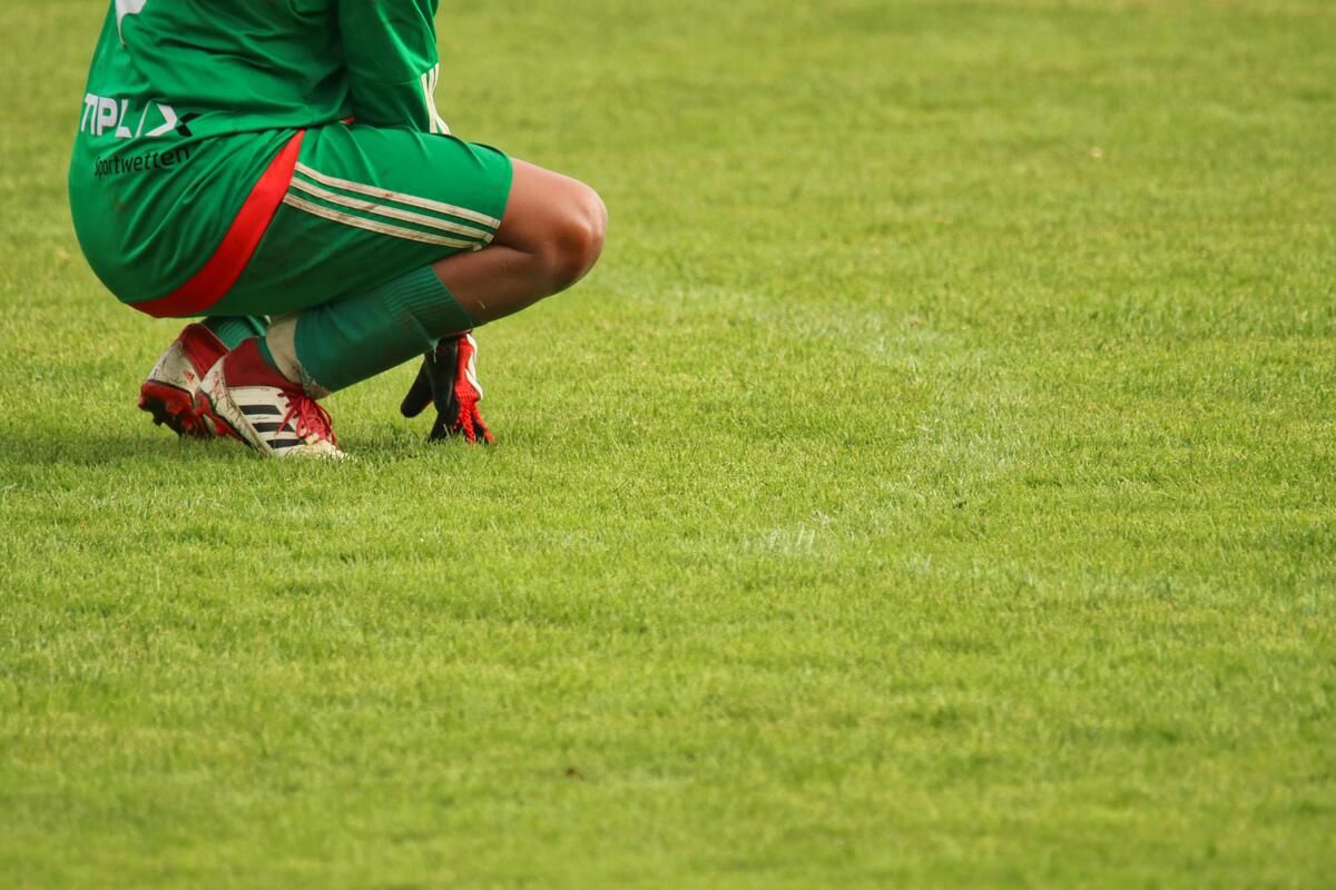 A soccer player in a green uniform is kneeling on a grassy field, possibly taking a break.