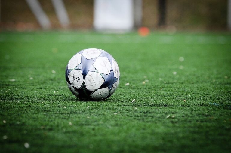 Ein Fußball mit blauen, weißen und schwarzen Flächen liegt auf einem grünen Feld. Der Hintergrund ist unscharf.