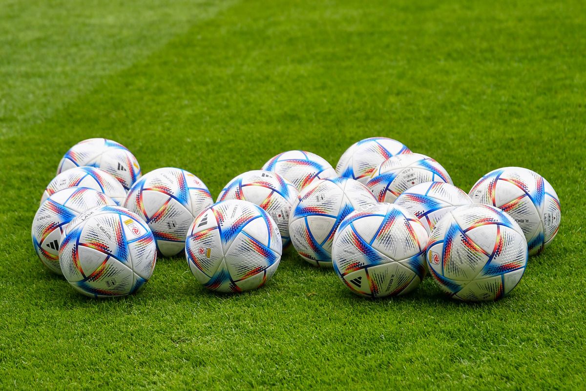 A collection of soccer balls with various designs are placed on a green grass field. The balls are in different sizes and colors, with some having logos.