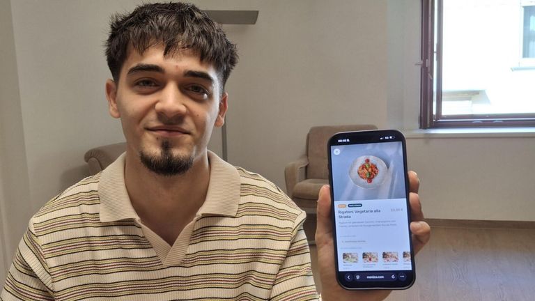 A man with a beard is smiling while holding a smartphone displaying a food menu.