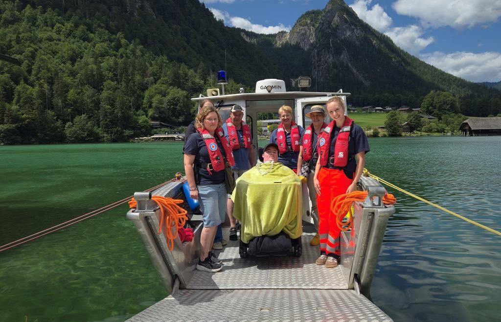 A group of people in life jackets on a boat with mountains and a lake in the background.
