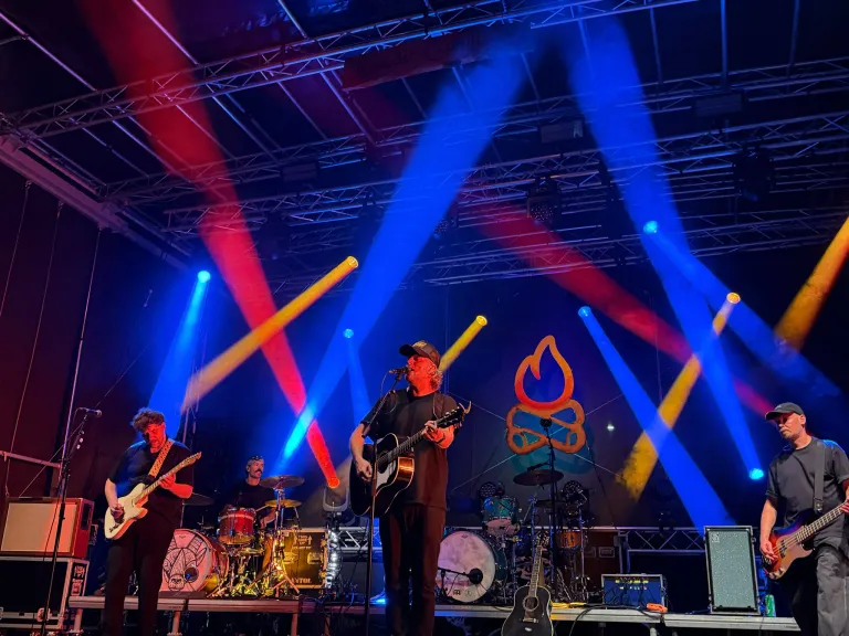 Eine Band tritt auf der Bühne unter leuchtendem blau-roten Licht auf, wobei ein Mitglied Gitarre spielt und in ein Mikrofon singt.
