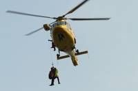 A person is being rescued by a yellow helicopter with a rope, flying in the sky.
