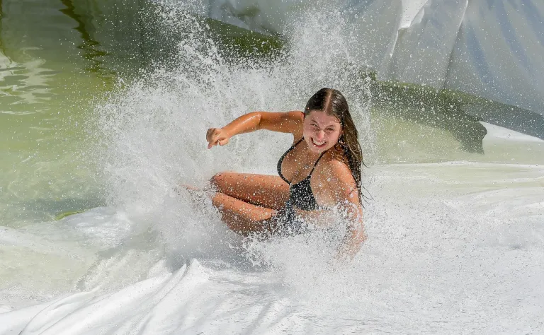 Eine junge Frau in einem schwarzen Bikini fährt auf einem Wasserrutsche eine Welle und genießt den Ritt mit einem Lächeln.