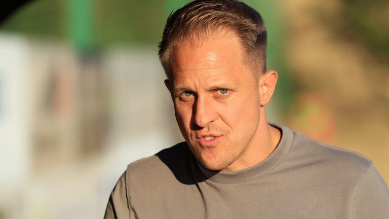 Ein Mann mit kurzen braunen Haaren und einem grauen T-Shirt schaut mit ernster Miene direkt in die Kamera.