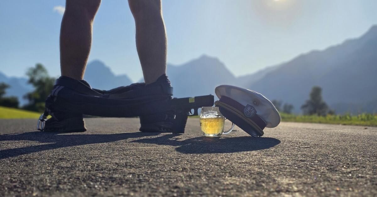 A person's legs in sneakers are shown with a gun, a hat, and a glass of beer on the ground.