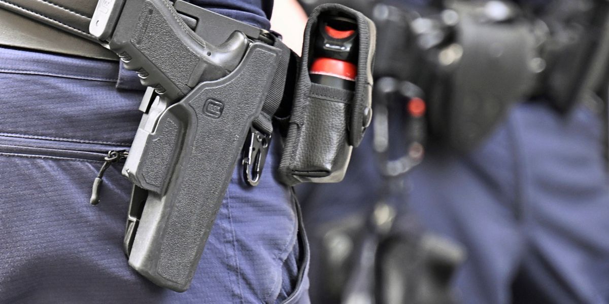A close-up view of a police officer's holstered handgun and pepper spray canister. The officer is dressed in blue uniform.