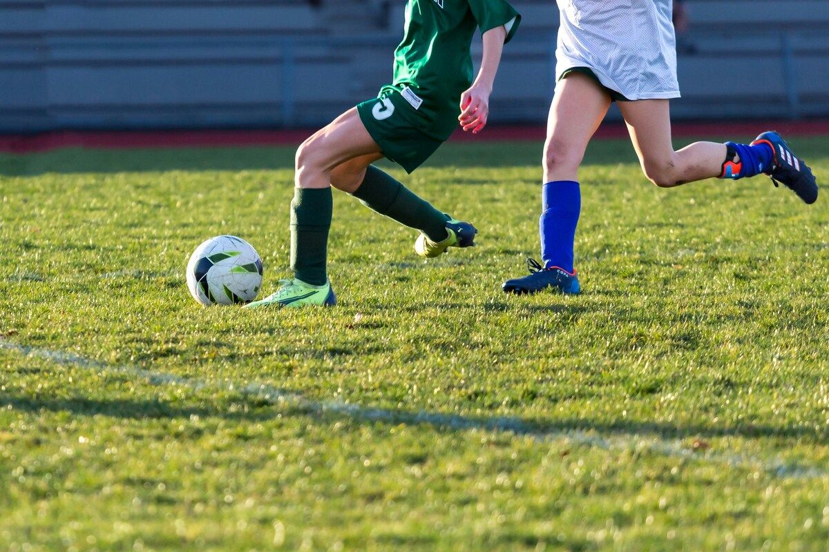 Two soccer players are on a field, one in green and the other in white, with the player in green about to kick the ball.