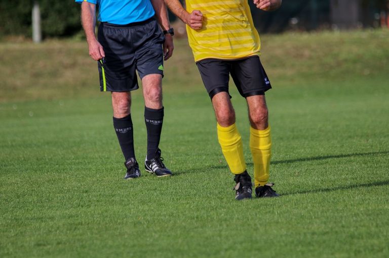 Two men on a soccer field, one in a yellow and black uniform, the other in a blue uniform.