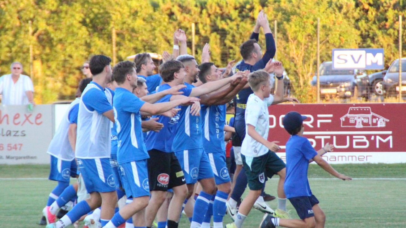 Eine Gruppe von Fußballspielern in blauen Trikots feiert mit einem jungen Jungen in Blau auf dem Feld.