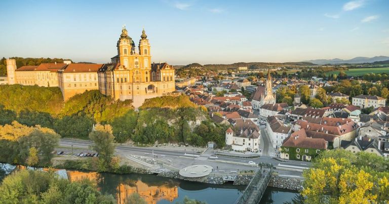 Ein Luftbild einer historischen Stadt mit einer großen Kirche, umgeben von Gebäuden, Bäumen und einem Fluss unter einem klaren Himmel.