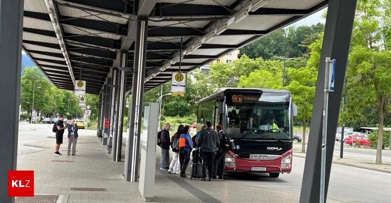 Eine Bushaltestelle mit wartenden Menschen. Der Bus ist rot und hat das Wort Postbus auf der Vorderseite.