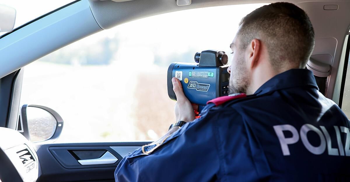 Ein Polizist im Auto misst mit einer Geschwindigkeitsmessgerät die Geschwindigkeit eines Fahrzeugs.