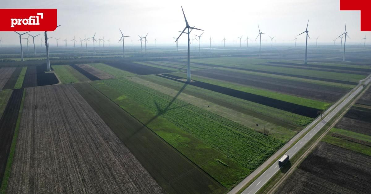 Aerial view of a vast wind farm with numerous wind turbines set against a backdrop of green fields and a road with a truck passing by.