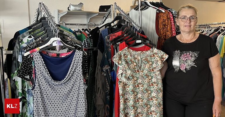 A woman stands next to a rack of various dresses, including floral and polka-dot patterns.