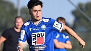 A soccer player in a blue jersey with the word 'Bau' on the front, running on the field.
