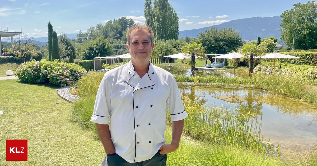 A man in a chef's uniform stands in a garden with a pond, smiling and posing for a photo.