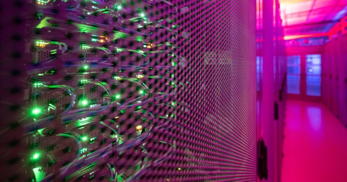 A close-up view of a server room with rows of servers, illuminated by green and purple lights, creating a vibrant and high-tech atmosphere.
