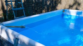 A clear blue inflatable pool with a hose filling it up on a sunny day.