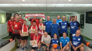 A group of people dressed in red and blue jerseys, some holding trophies, posing for a photo in a sports hall.