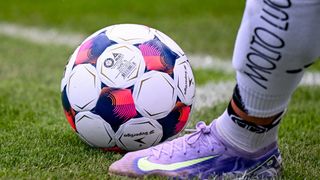 A close-up of a soccer ball with a Nike player's foot nearby on a field.