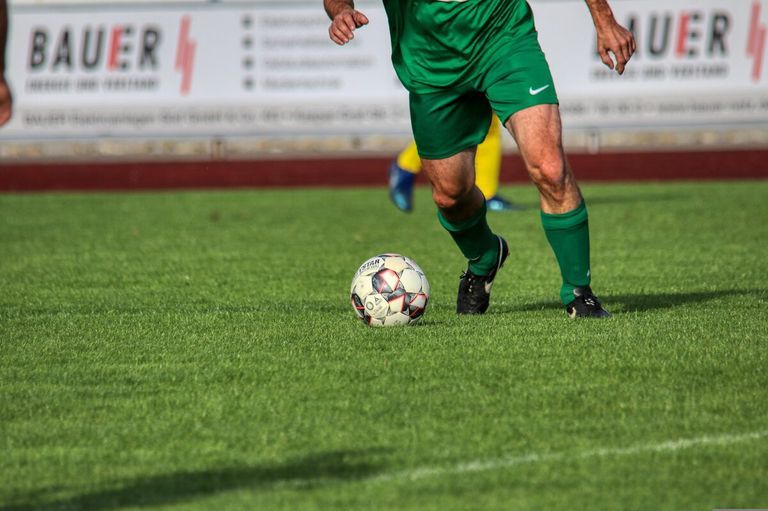 Ein Fußballspieler in grüner Uniform tritt einen Fußball auf einem grünen Feld.